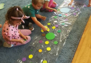 Dzieci w dowolny sposób układają kropki na foli.